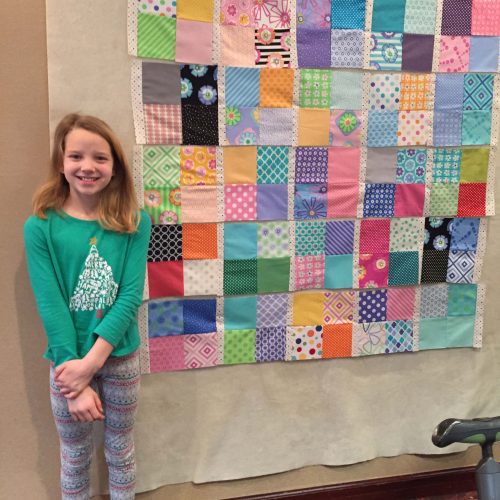 Young quilter posing next to a quilt.
